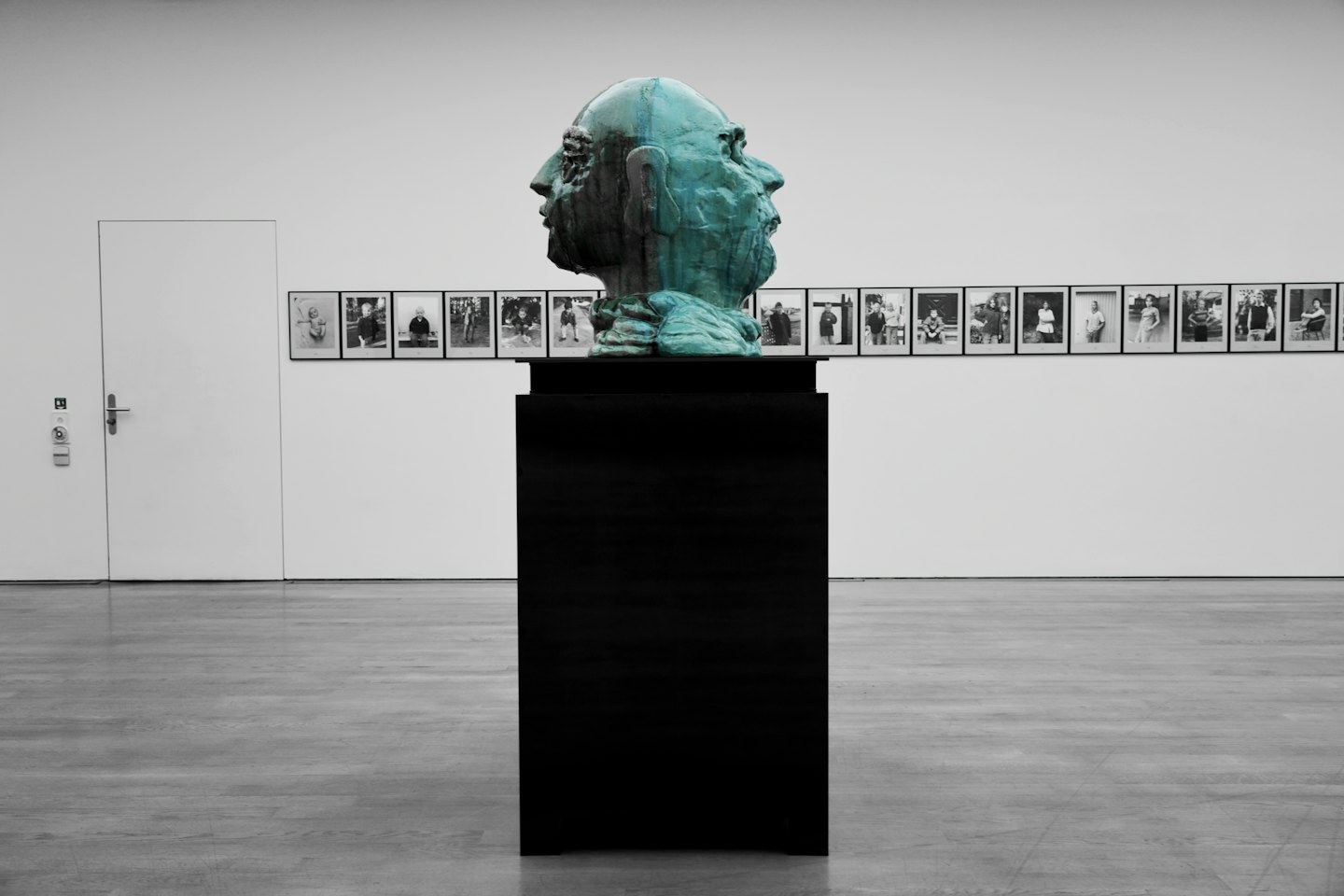 Bronzen hoofdsculptuur met groene patina op een zwart voetstuk in een kunstgalerie.