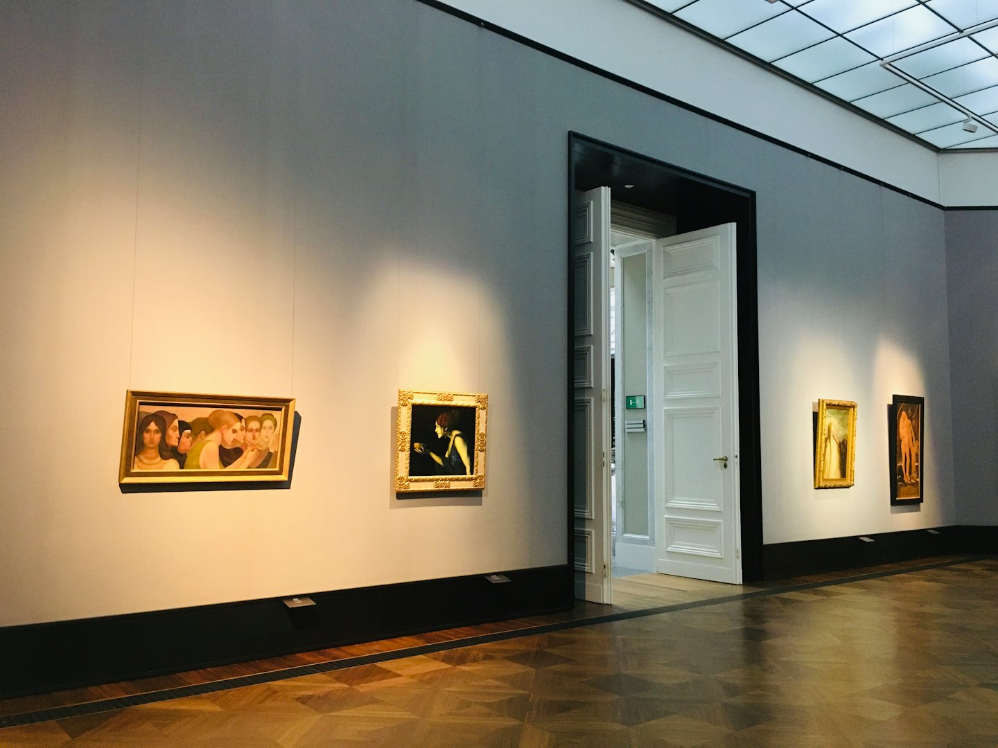 Lijsten met schilderijen hangen aan de muren in een lege kunstgalerie.