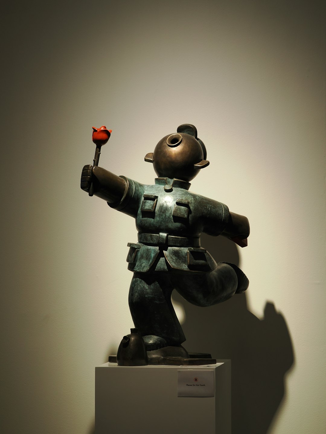 Bronzen beeld van een figuur met een rode roos op een sokkel.